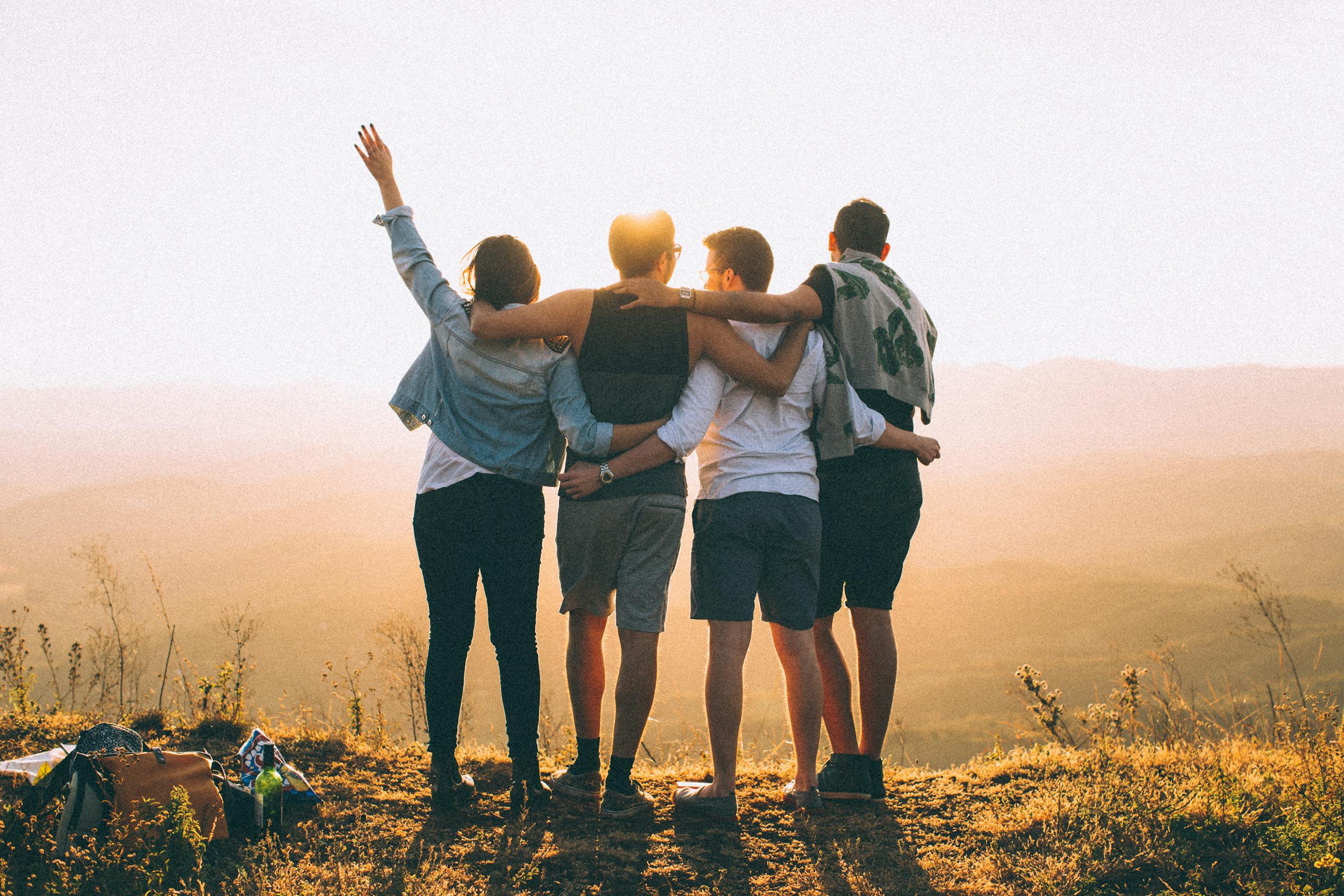 A group of friends embrace while enjoying a sunset view from the mountain top.