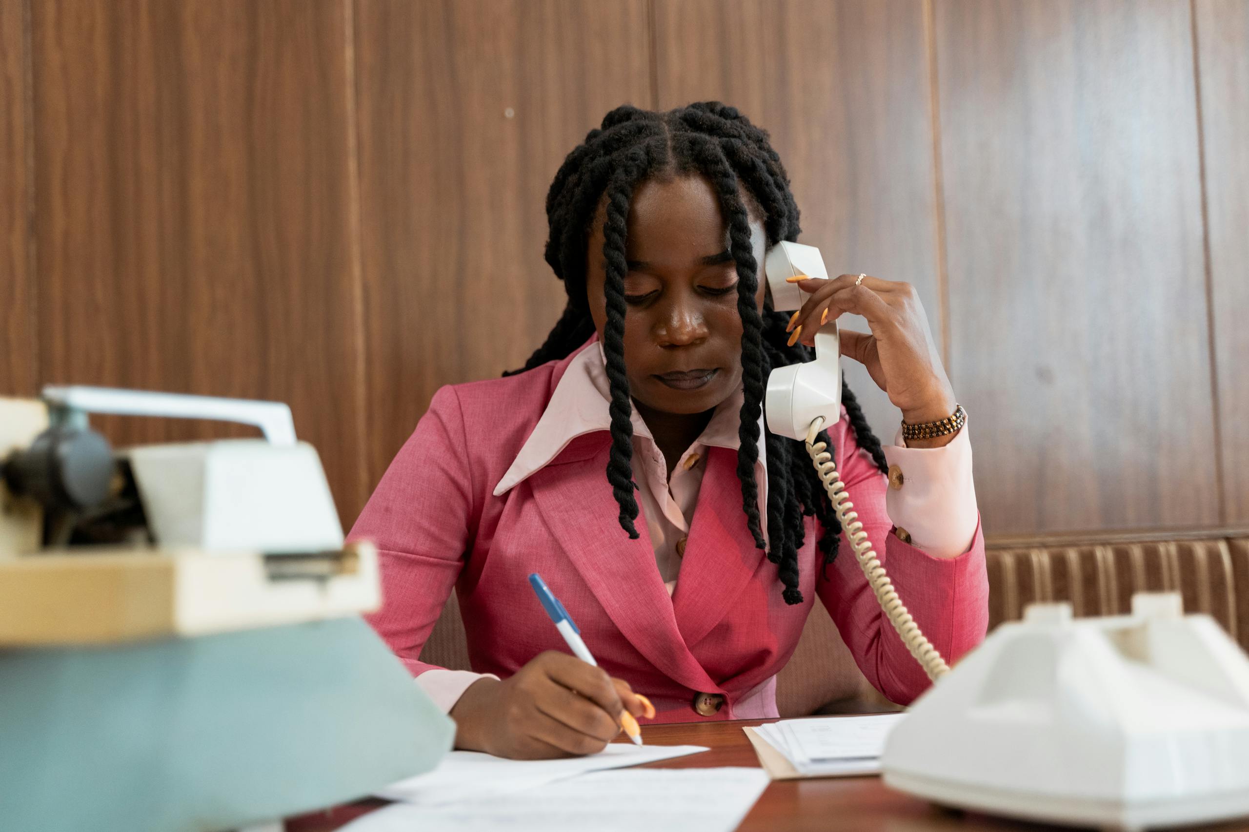 Professional woman in 80s style business attire making notes during a phone call.